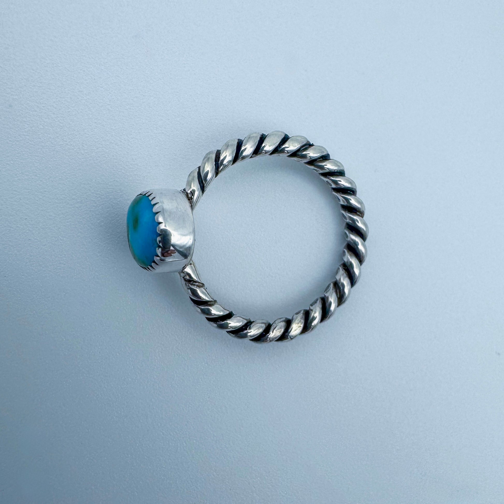 Silver ring with a turquoise blue stone on a light gray background