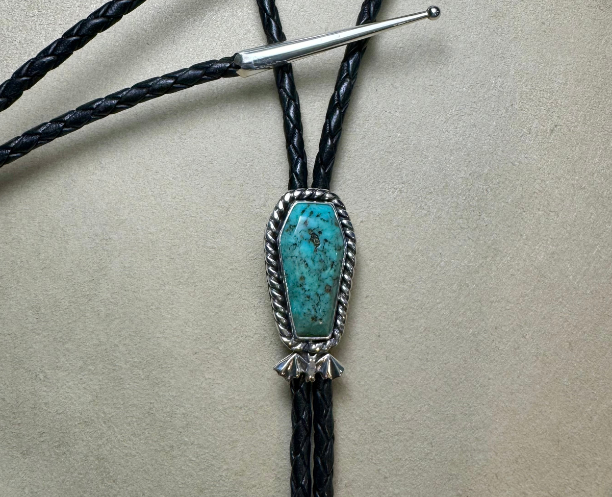 Bolo tie with turquoise stone and silver clasp on a beige background